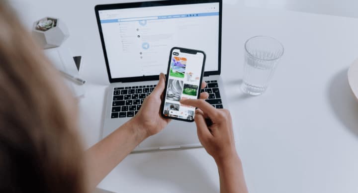 Person browsing on a smartphone with a laptop open in the background